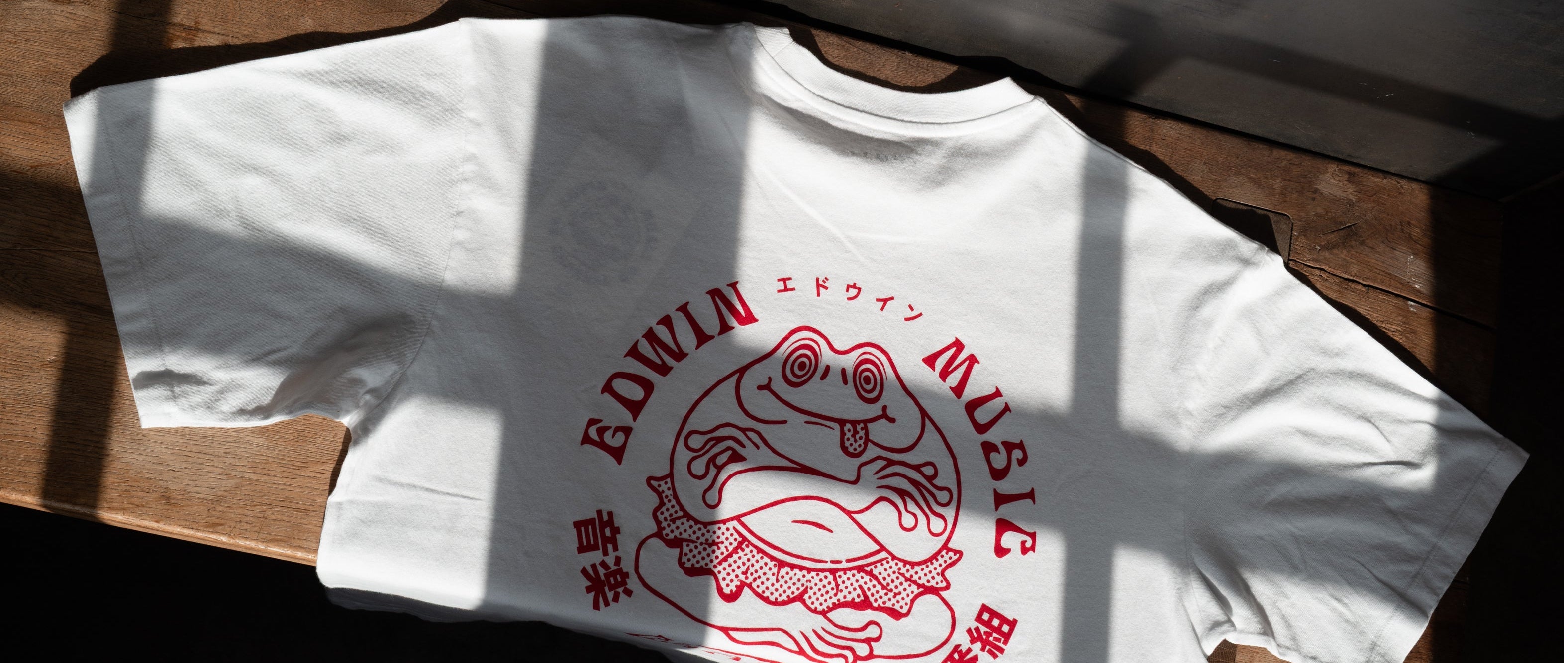 weißes Edwin T-Shirt mit rotem Backprint liegt auf Holzbank