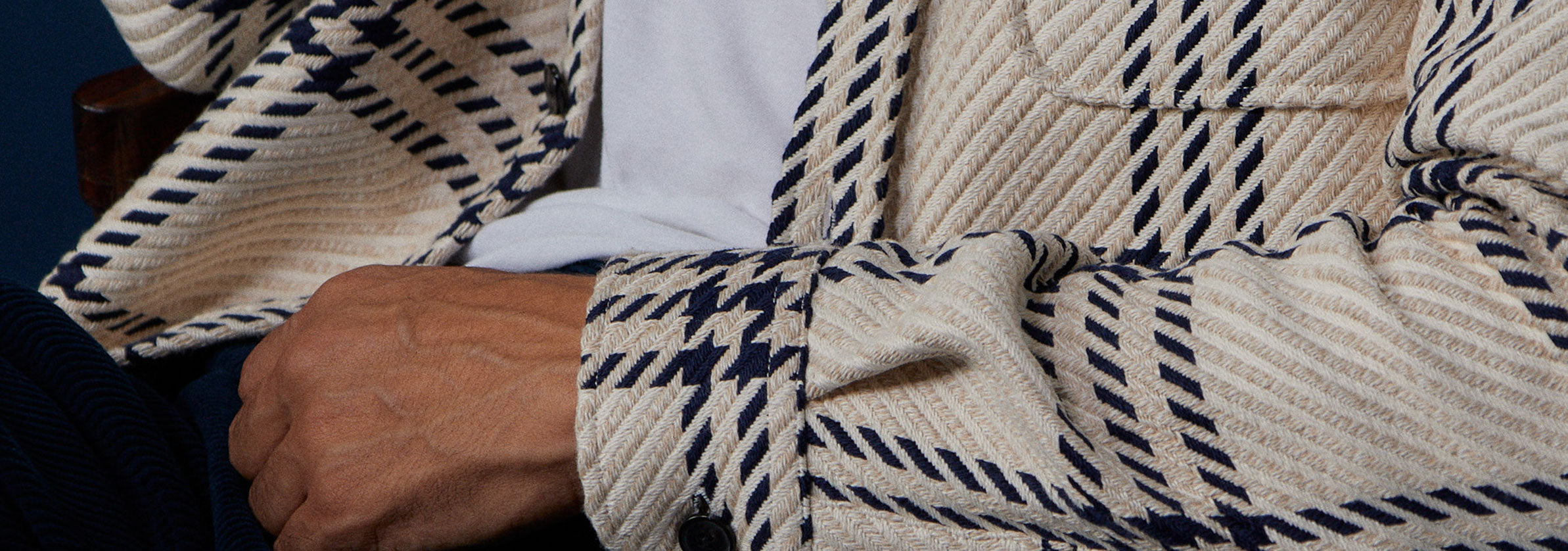 Ein sitzender Mann trägt ein Portuguese Flannel Hemd in den Farben creme, blau.